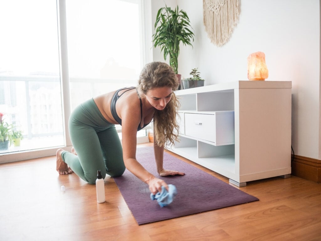 Yogalehrerin putzt eine Yogamatte in ihrem eigenen Yoga Studio