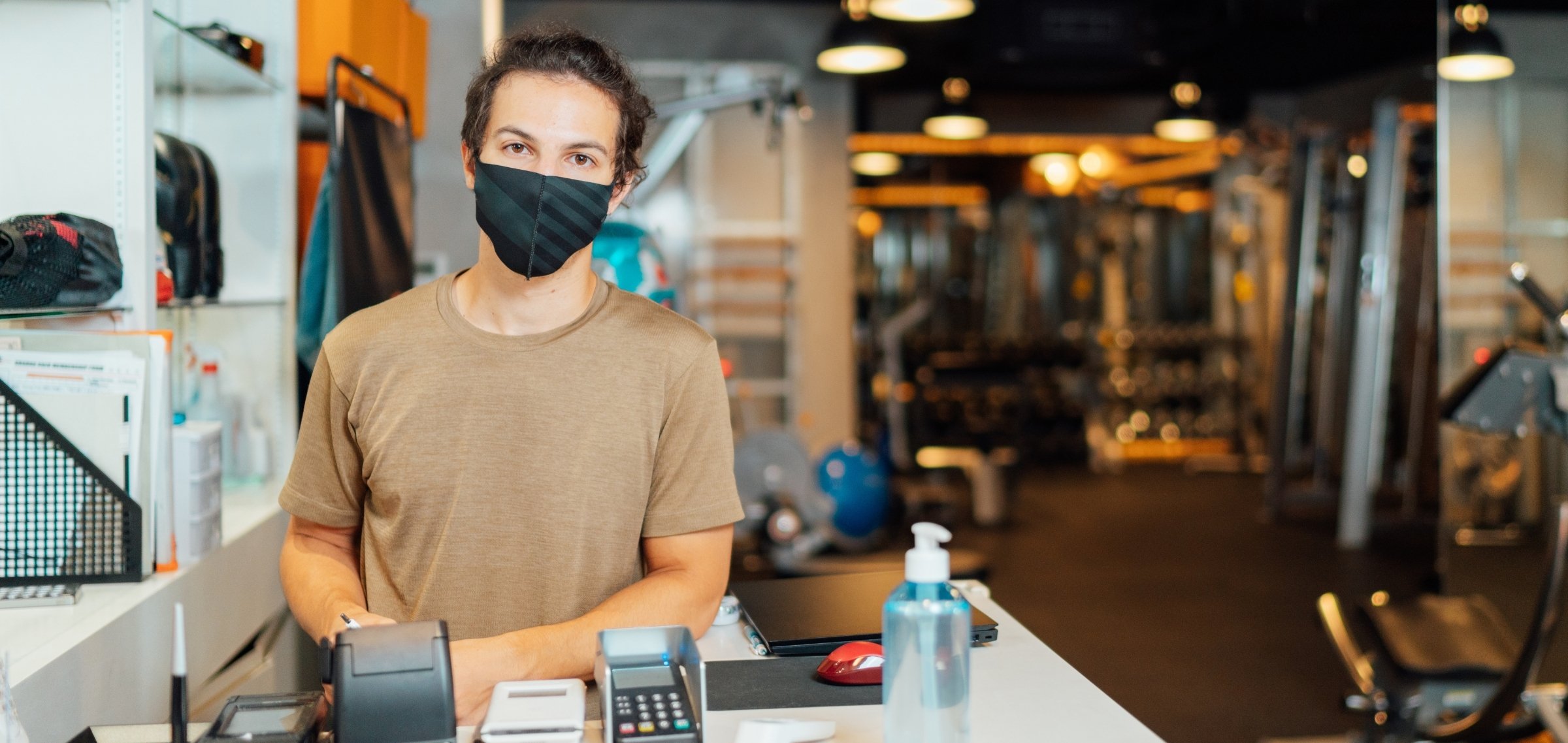 Mann mit Maske hinter Check-In-Schalter eines Studios - TSE Kasse für Studios und Sportstätten