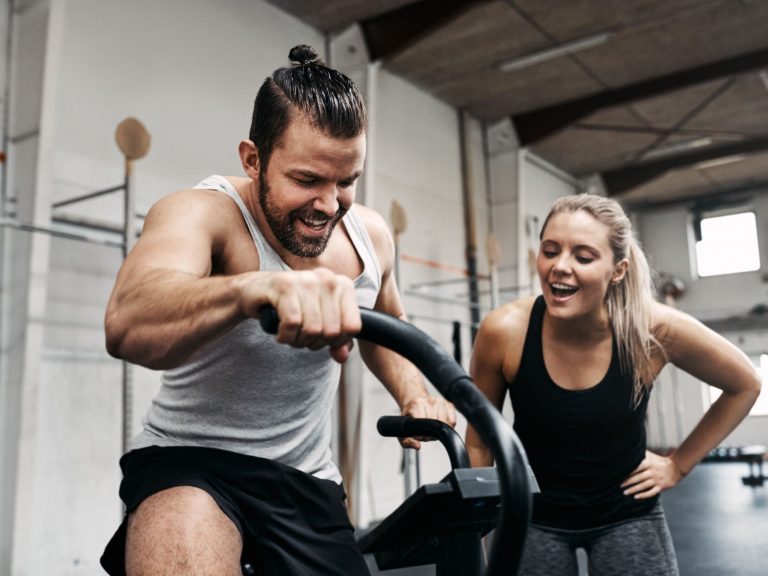 mann trainiert auf hometrainer. eine frau steht daneben und feuert ihn an!