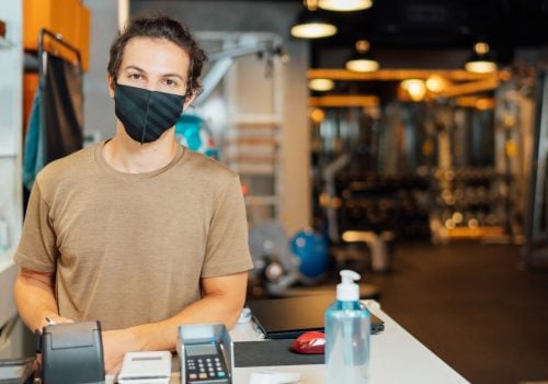 Mann mit Maske hinter Check-In-Schalter eines Studios - TSE Kasse für Studios und Sportstätten